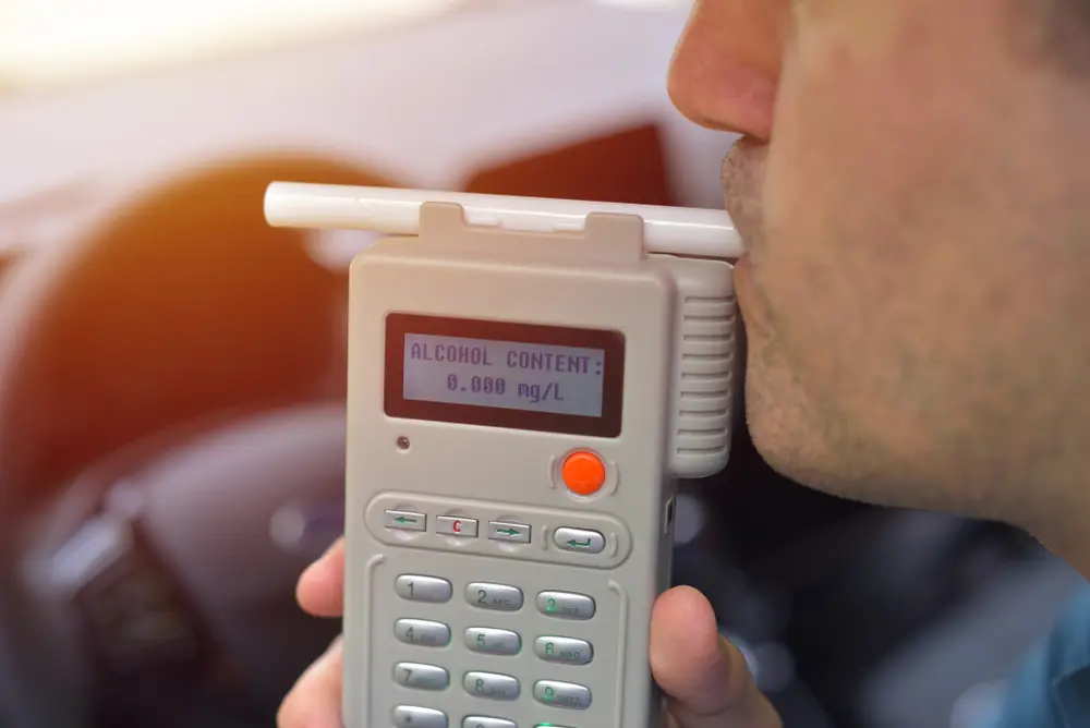 Man using a breathalyzer device showing an alcohol content reading of 0.000 mg/L, emphasizing DUI testing context.