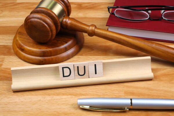 Gavel and wooden block with "DUI" letters, legal books, and glasses, symbolizing DUI defense and legal services.