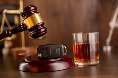 Gavel, car keys, and a glass of alcohol symbolizing legal implications of DWI charges and their impact on driving privileges.