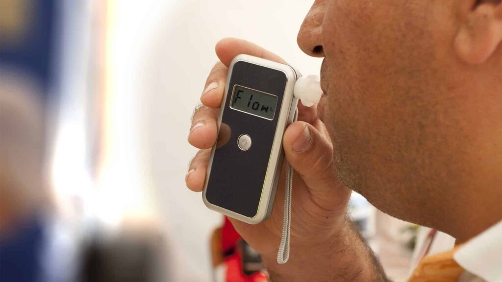 Person using a breathalyzer device to measure blood alcohol concentration, relevant to DWI legal limits in Texas.