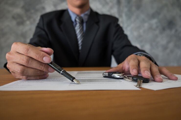 Businessman in a suit holding a pen over legal documents with car keys on a table, representing DUI legal matters and client consultations.