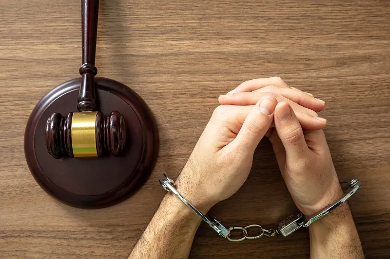 Hands in handcuffs resting on a wooden table beside a gavel, symbolizing legal consequences of DWI charges.