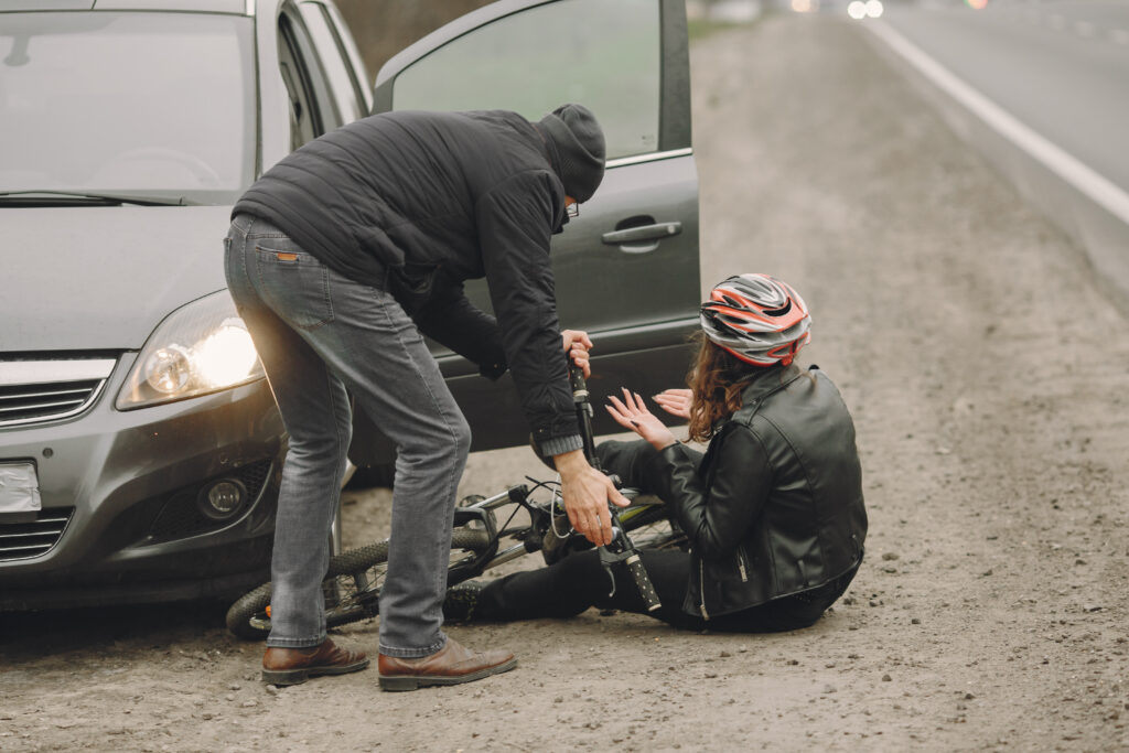 Man assisting a woman in a helmet after a scooter accident near a car on a roadside, highlighting the risks of impaired scooter riding.