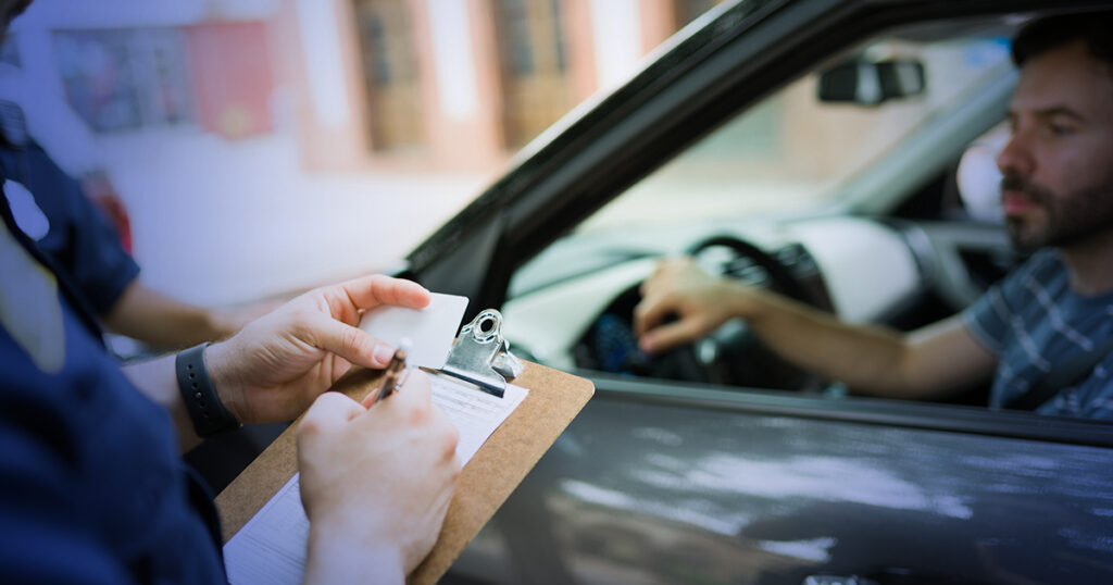 Police officer conducting a traffic stop, writing on a clipboard while the driver, appearing concerned, sits in the car, relevant to DWI investigations in Texas.