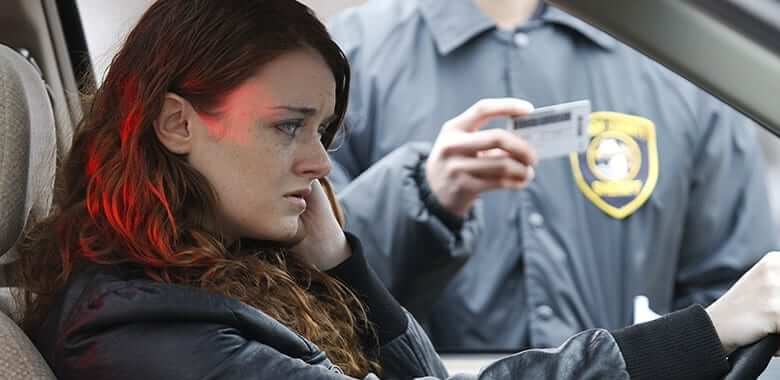 Woman in a car looking distressed as a police officer approaches with a driver's license, illustrating DUI arrest scenario relevant to Texas DUI penalties.