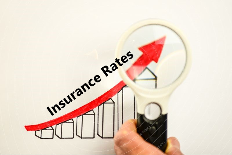 Hand holding magnifying glass over a graph with an upward trend, emphasizing the text "Insurance Rates," illustrating the impact of DUI on insurance premiums.