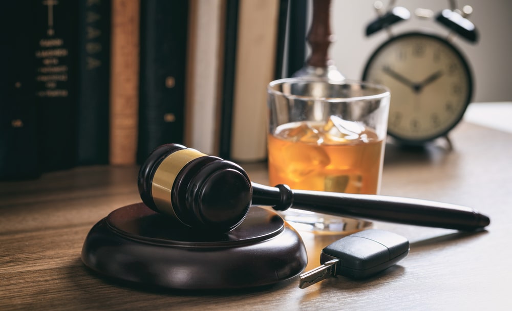 Gavel on wooden block with whiskey glass and car key, symbolizing DUI legal issues and defense in Texas.
