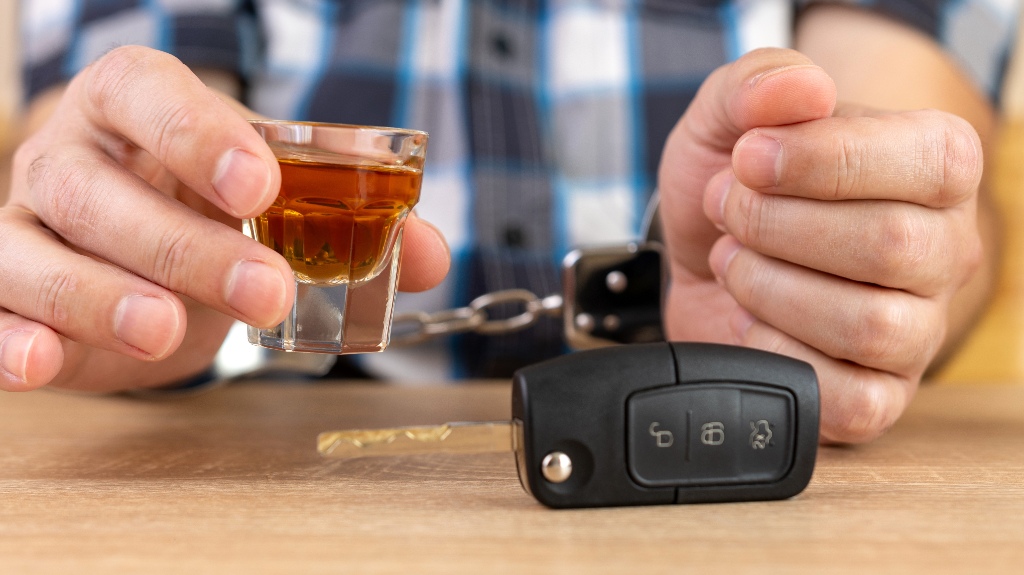 Person holding a shot glass of alcohol with car keys and handcuffs on a table, illustrating the consequences of DUI arrests in Texas.