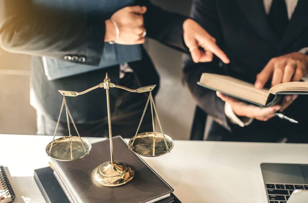 Scales of justice in foreground with two attorneys discussing legal strategies over a book, symbolizing DUI defense and legal representation.