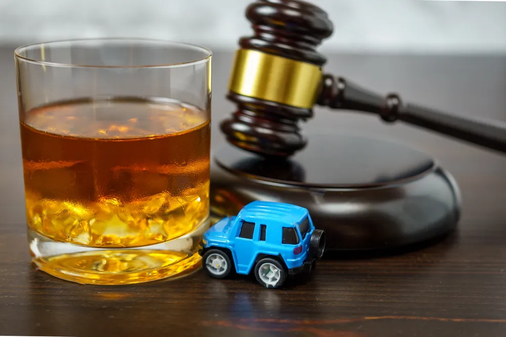 Glass of whiskey, toy car, and gavel symbolizing DUI legal issues and courtroom proceedings in Texas.
