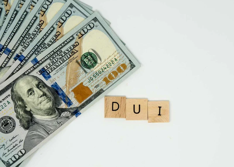 Stack of hundred dollar bills with wooden blocks spelling "DUI," symbolizing the financial costs associated with DUI charges.