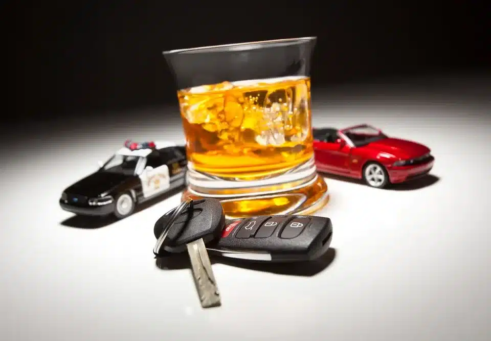 Glass of whiskey with ice, car keys, toy police car, and toy sports car, illustrating the consequences of DUI in Texas.