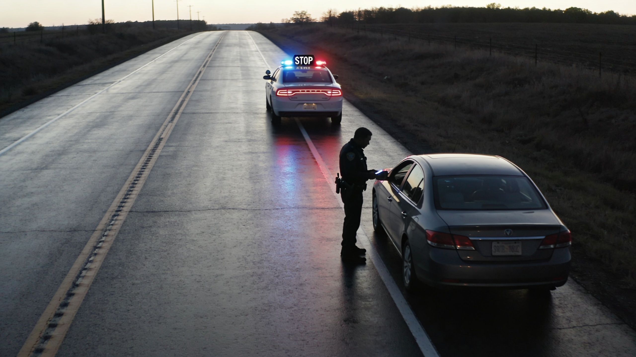 A police officer talks to a driver through the window of a silver sedan during a roadside traffic stop.